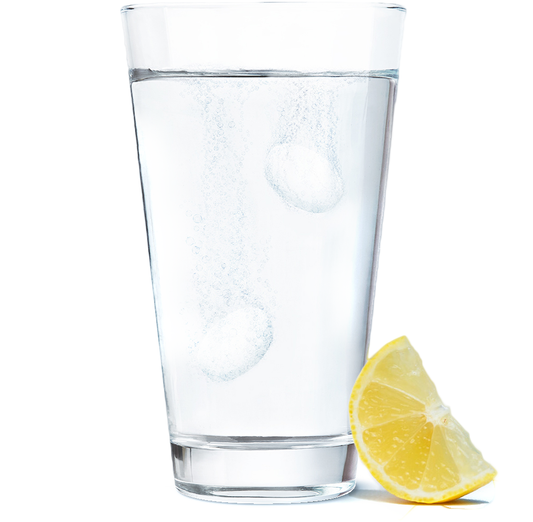 Glass of water with Blowfish tablets inside of it and a fresh hydrating lemon slice next to it. 